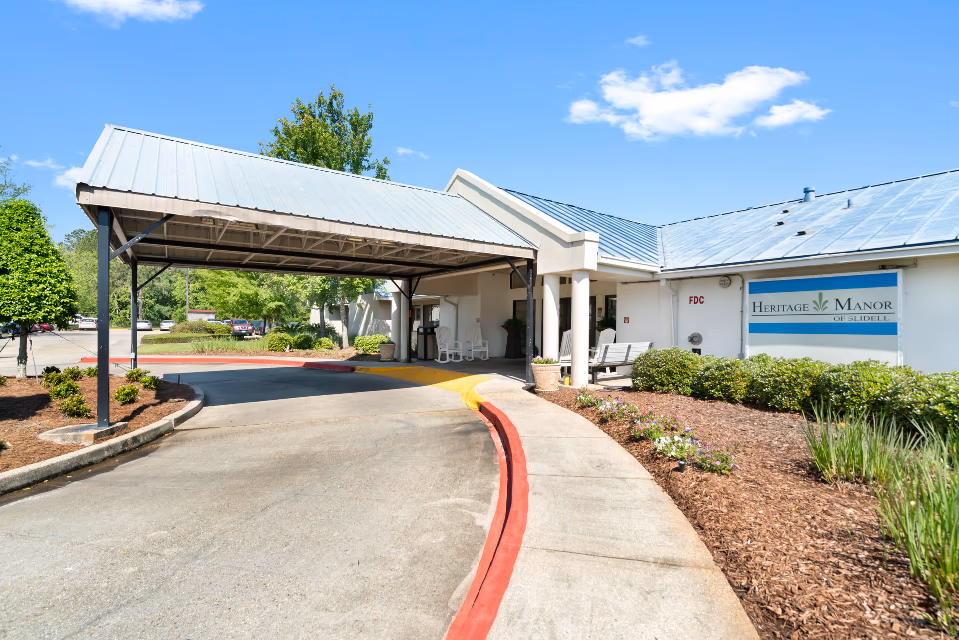 Covered drive-up entrance and landscaped front of Heritage Manor of Slidell with a canopy and visible facility sign.