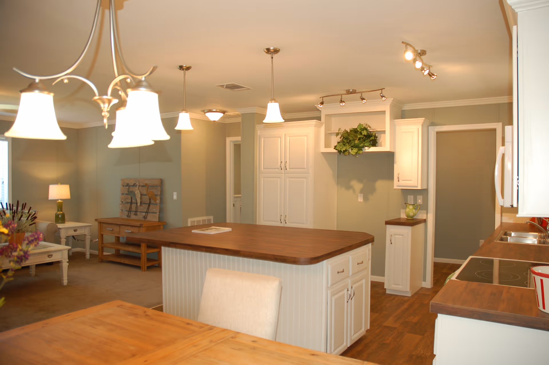 Open-concept kitchen with a central wooden island, white cabinets, pendant lights, and an adjacent living area.