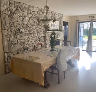 Stone-walled dining area with a long plastic-covered table and chairs near sliding glass doors.