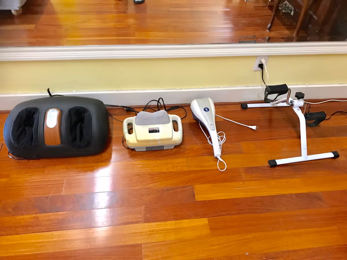Four different foot and leg exercise and massage devices placed on a wooden floor in front of a wall with a large mirror.