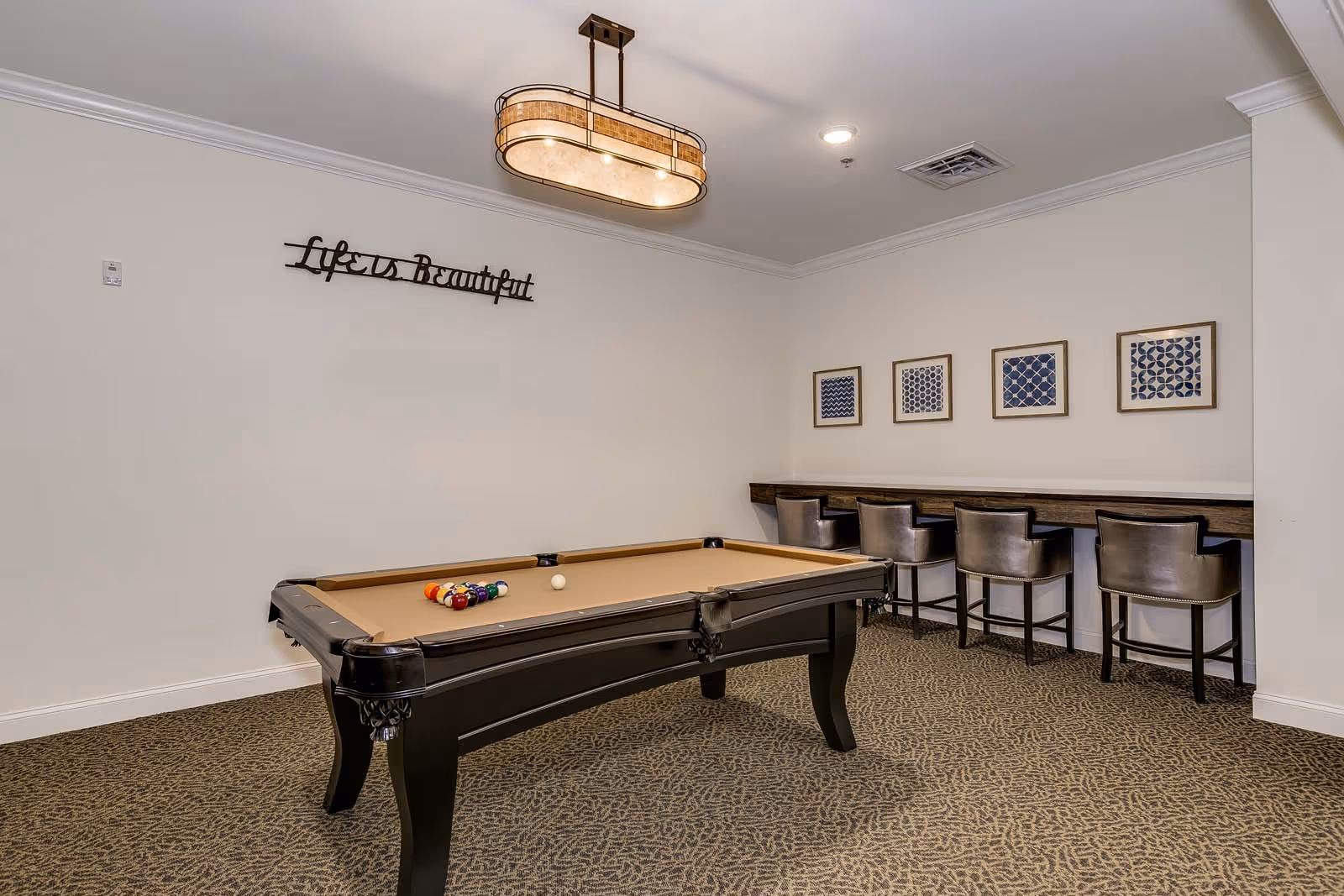 Recreation room with a pool table, bar-height counter and stools, framed artwork, and a 'Life is Beautiful' wall sign.