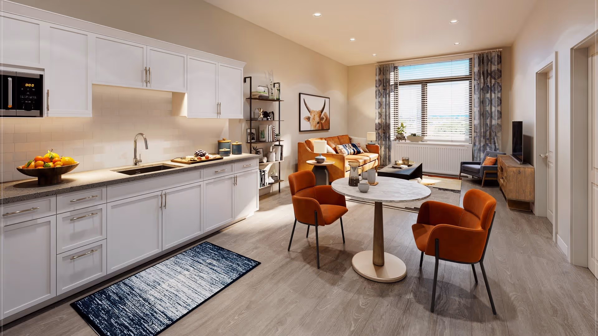 A bright and modern open-concept living space featuring a kitchen area with white cabinets, a sink, and a microwave. In front of the kitchen is a small round dining table with two orange chairs. The living area includes an orange sofa, a coffee table, a TV on a wooden stand, and a large window with patterned curtains allowing natural light to fill the room. Decorative items and artwork adorn the walls and shelves.