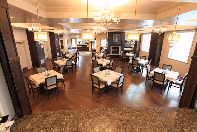 Spacious elegant dining room with multiple set tables, chandeliers, and a central fireplace.