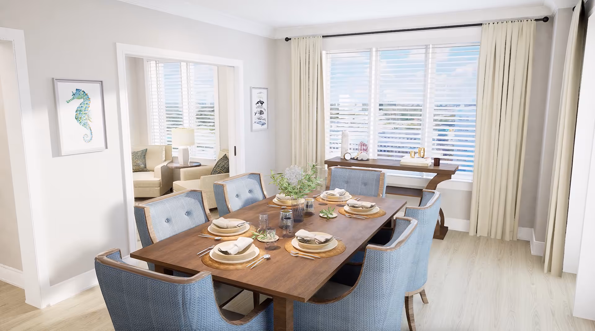 A bright dining room with a wooden table set for six, featuring blue upholstered chairs. The table is decorated with plates, napkins, cutlery, glasses, and small plants. Large windows with white blinds and cream curtains allow natural light to fill the room. A console table with decorative items is placed against the wall under the window. Adjacent to the dining room is a living area with beige armchairs and a lamp, visible through an open doorway.