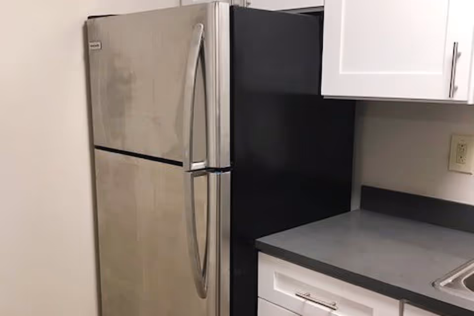 Stainless steel top-freezer refrigerator next to a gray countertop and white kitchen cabinets.