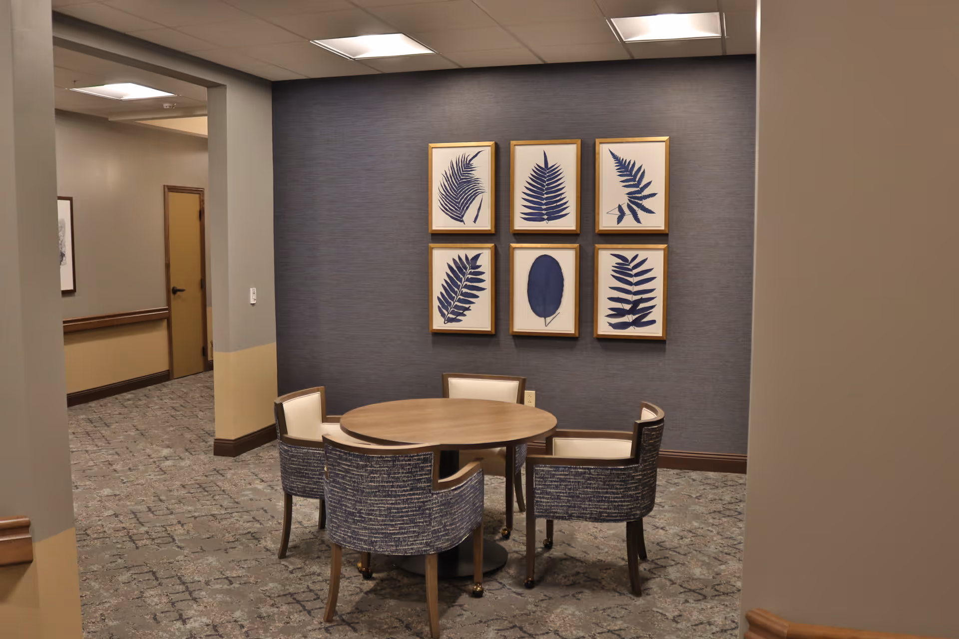 Small interior seating area with a round table, four chairs, and six framed blue botanical prints on a gray accent wall.