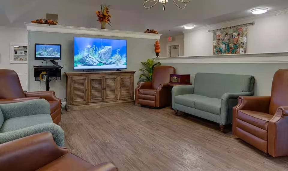 A comfortable common lounge with a green loveseat and brown leather chairs facing a large TV on a wooden console.