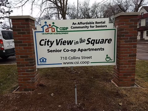 Outdoor sign mounted between two brick pillars reading "City View in the Square Senior Co-op Apartments" with address and wheelchair symbol.