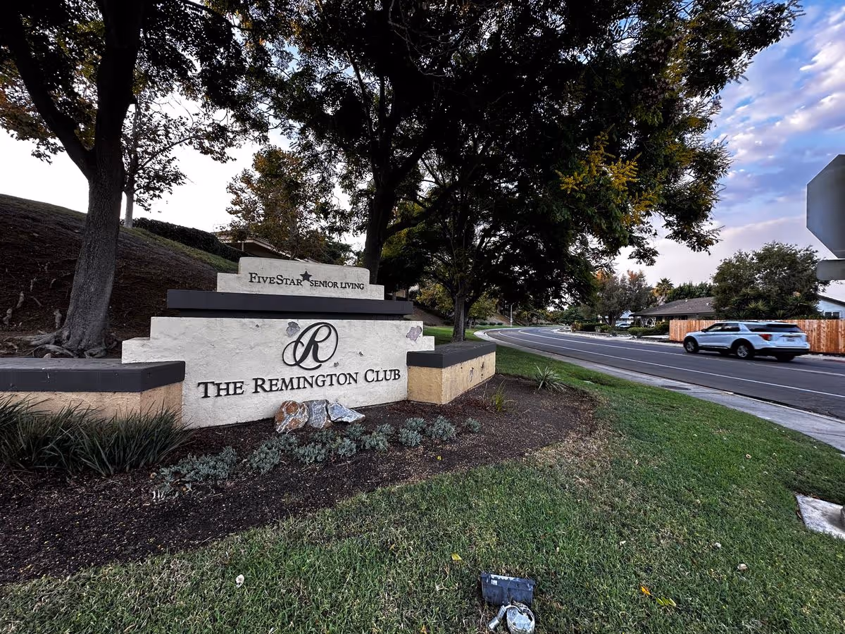 Entrance sign for The Remington Club and Five Star Senior Living on a landscaped lawn next to a street with trees and a car passing by.