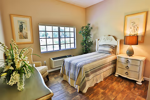 Sunlit single bedroom with a twin bed, nightstand and window overlooking greenery.