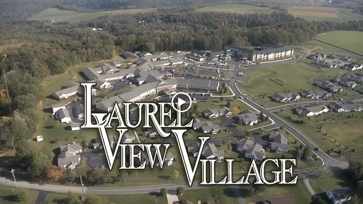 Aerial view of Laurel View Village, showing multiple buildings, roads, and green spaces surrounded by trees and fields.