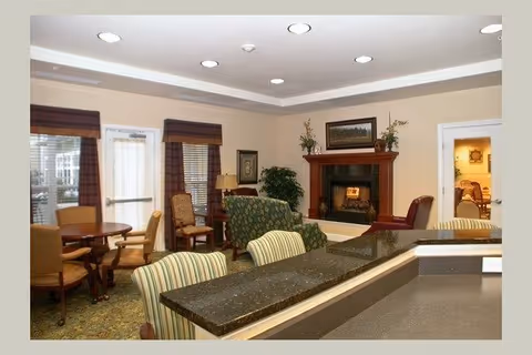 Communal living area with upholstered chairs, a fireplace, a dining table, and a granite-topped counter.