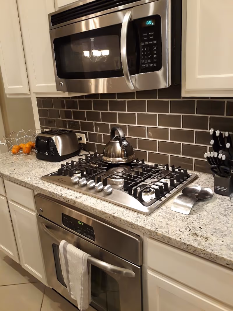 Modern kitchen with a stainless steel gas cooktop and oven, microwave, kettle, toaster, and granite countertop.