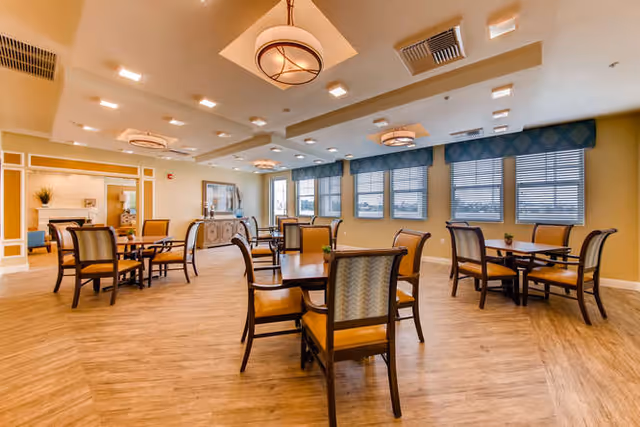 Spacious dining room with multiple tables and chairs, pendant lights, large windows, and wood flooring.