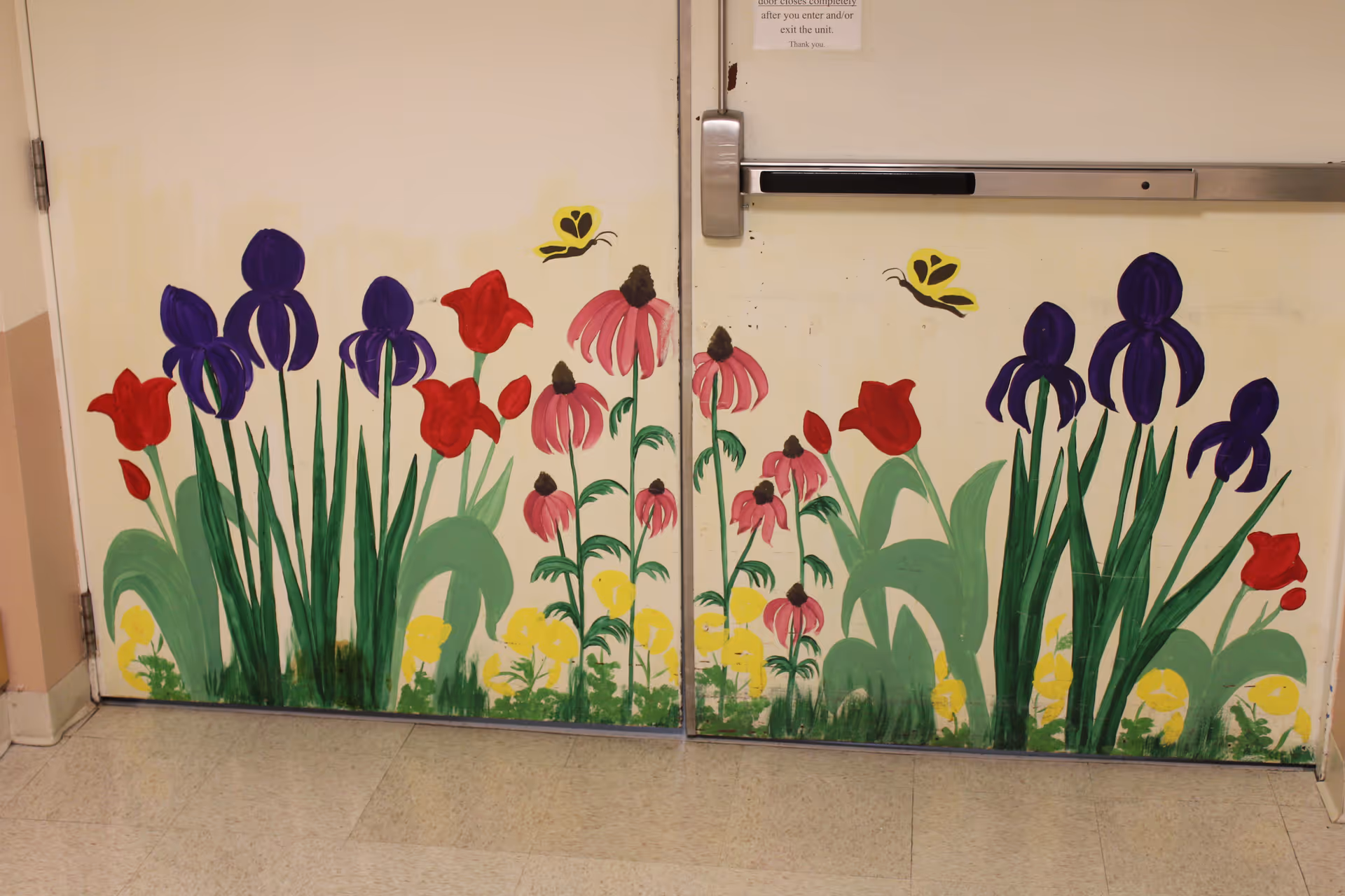 Double doors painted with colorful flowers including purple irises, red tulips, pink coneflowers, and yellow flowers, along with two yellow butterflies near the top of the doors.