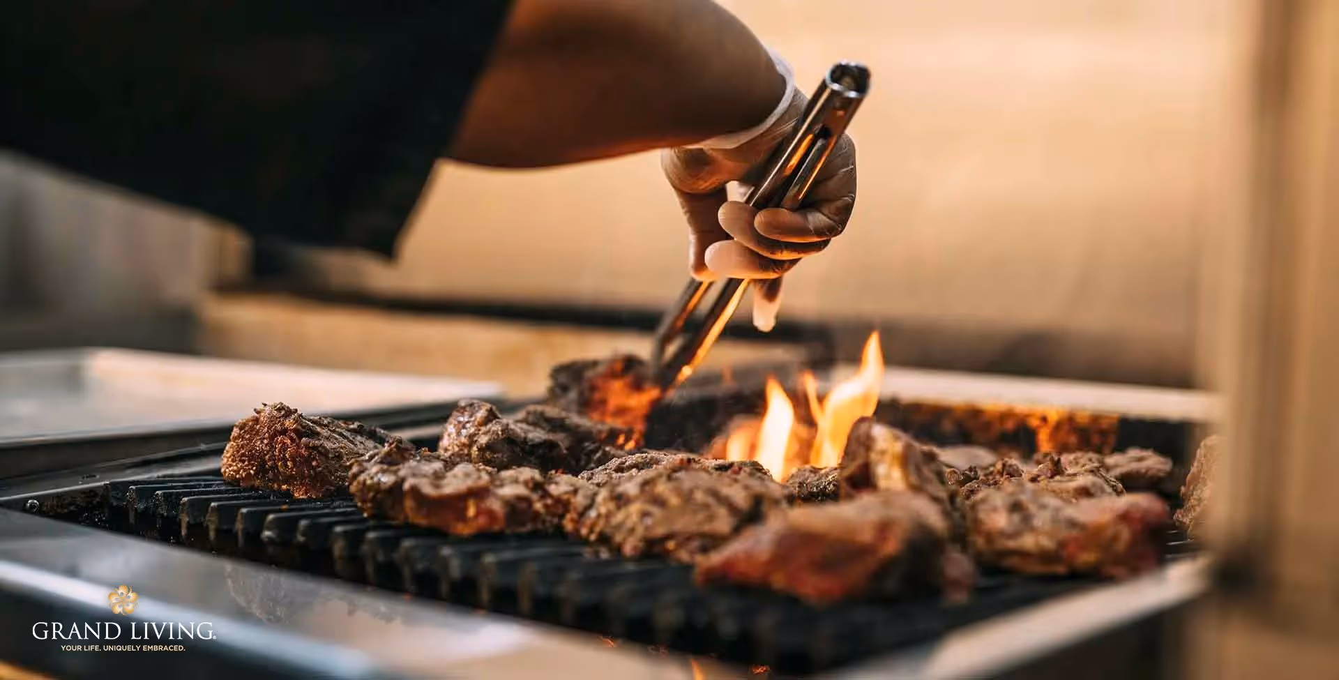 A person using tongs to grill several steaks over an open flame on a grill.