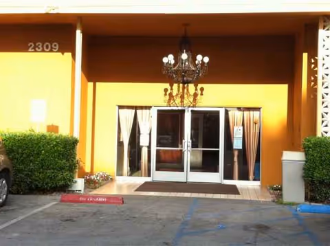 Orange building entrance with glass doors, chandelier, and greenery at Santa Fe Heights Healthcare Center.