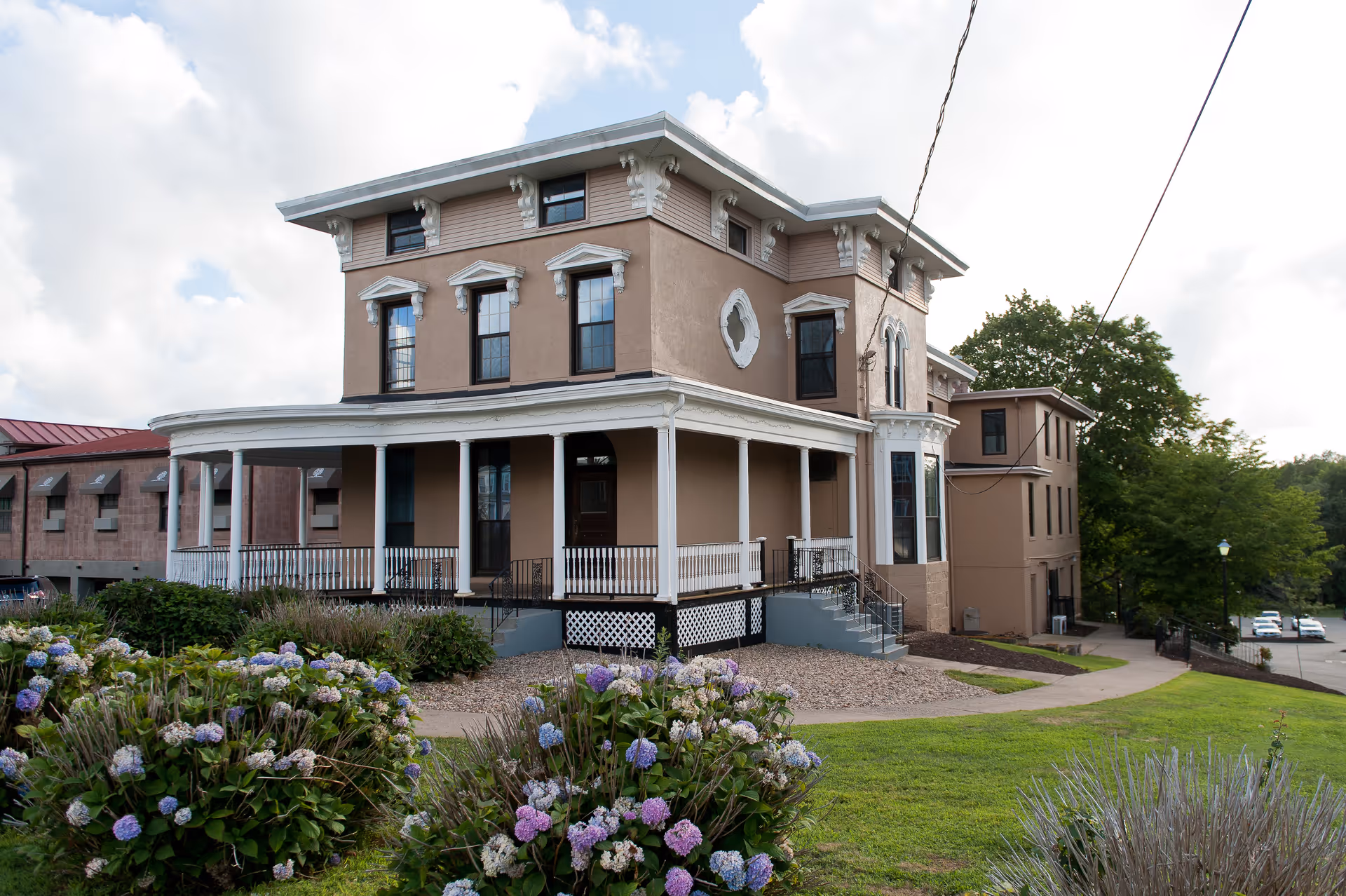 Front exterior of a multi-story historic-style building with a wraparound porch and flowering hydrangea bushes in the foreground.