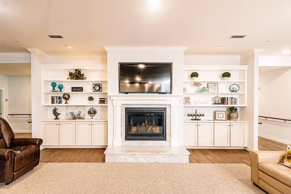 Bright common living room with a central fireplace and wall-mounted TV flanked by built-in shelves and seating.