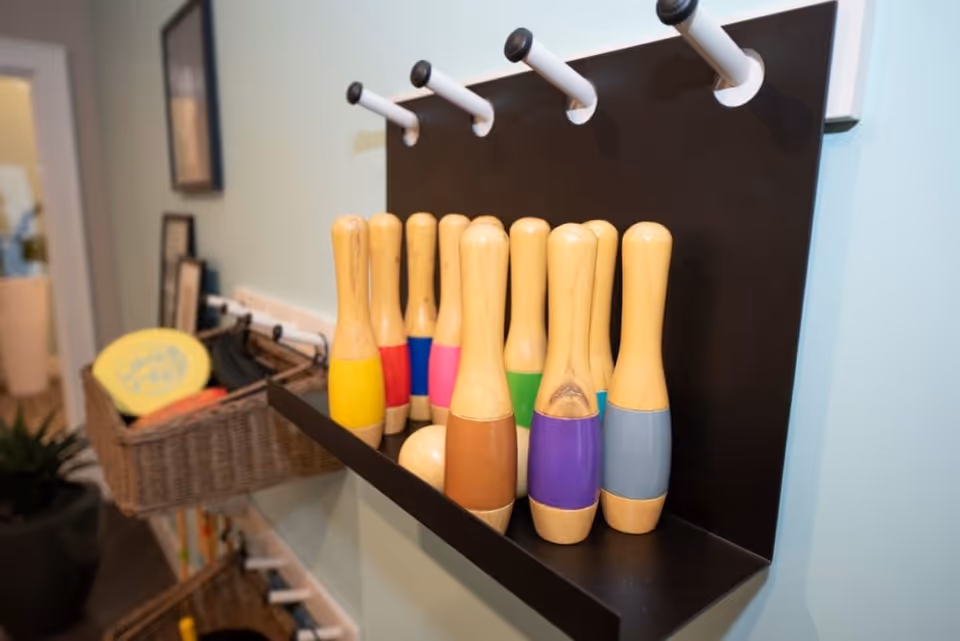 Colorful wooden toy bowling pins arranged on a black wall-mounted shelf against a light blue wall in an interior room.