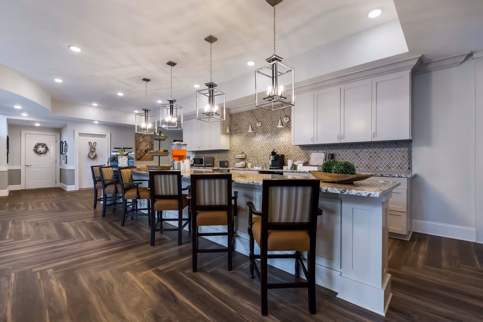 Spacious communal kitchen area with a long marble island, bar stools, pendant lights, and white cabinetry.