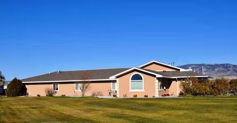 Single-story peach-colored senior living facility with lawn and blue sky.