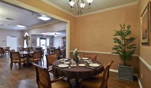 Interior dining room with round tables set for a meal, chairs, chandelier, and a potted plant.