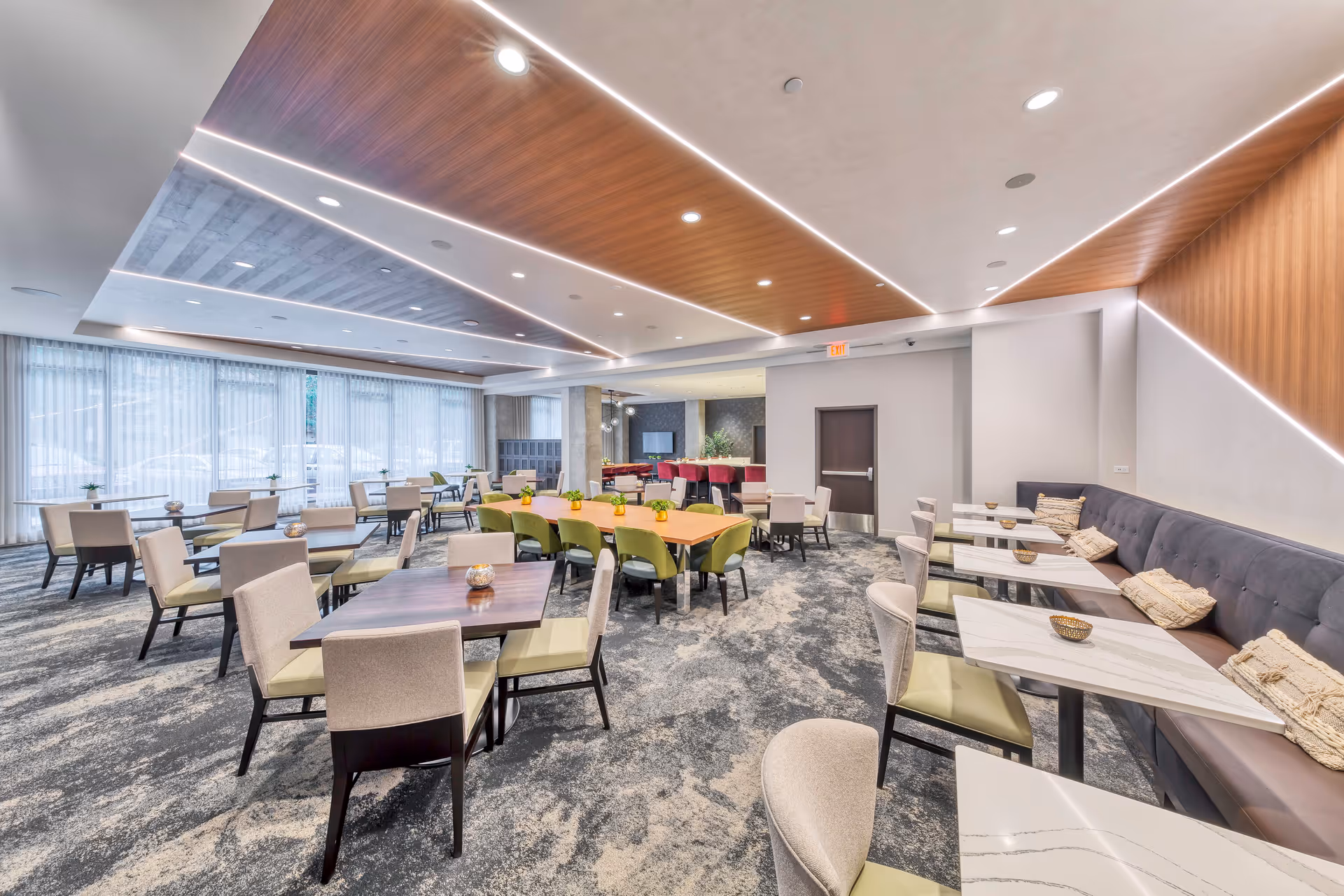 Bright modern communal dining and lounge area with multiple tables, chairs, banquette seating and large windows.