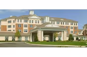 Front exterior of a multi-story senior living building with a covered porte-cochère entrance and landscaped driveway.