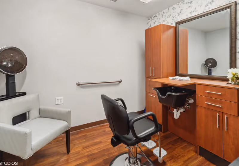 Small hair salon room with a styling chair, sink, mirror, wooden cabinets and a hooded hair dryer.