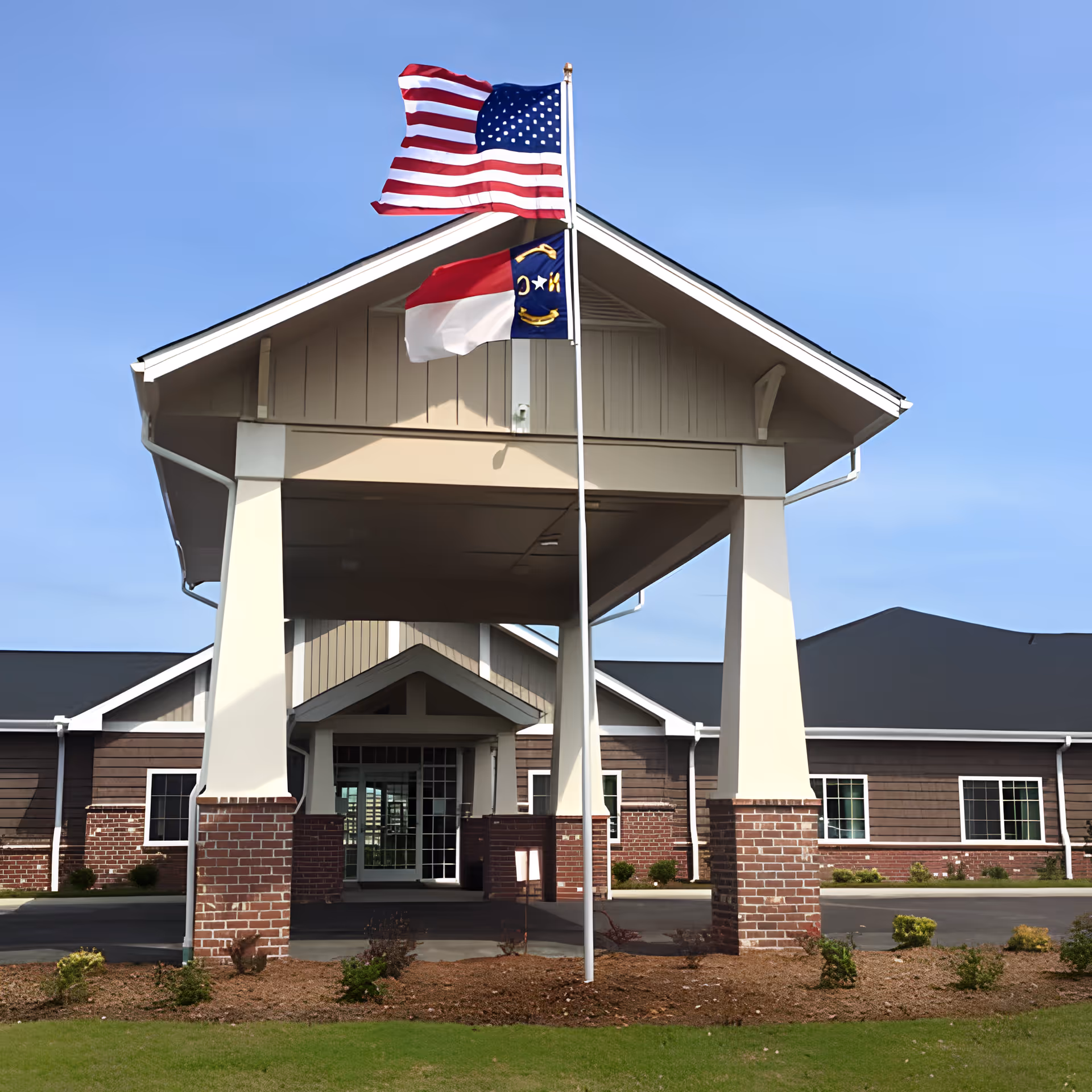 Front entrance of a building with a covered portico, brick columns, and American and state flags flying on a flagpole.