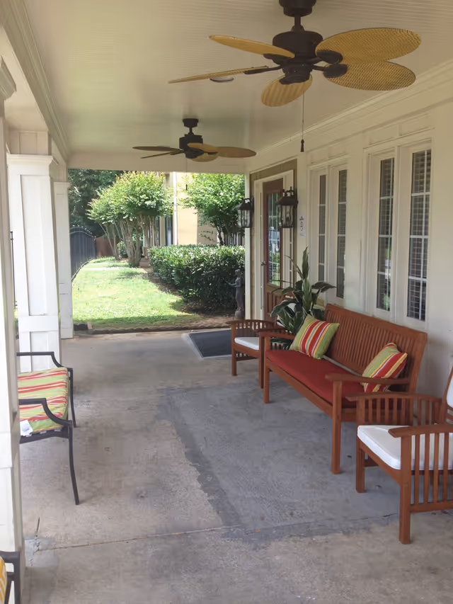 Covered porch with wooden bench seating, ceiling fans, and a view of a small lawn and walkway.