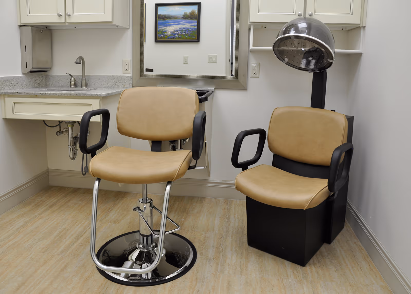 Salon treatment room with beige styling chairs, sink, and a hair dryer hood.
