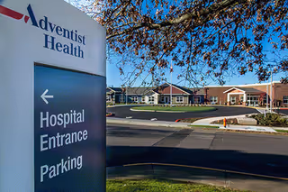 Adventist Health sign for hospital entrance parking with campus buildings in background.