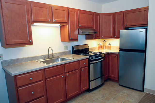 Kitchen with cherry wood cabinets, laminate countertops, a stainless steel refrigerator and gas stove, and a sink.