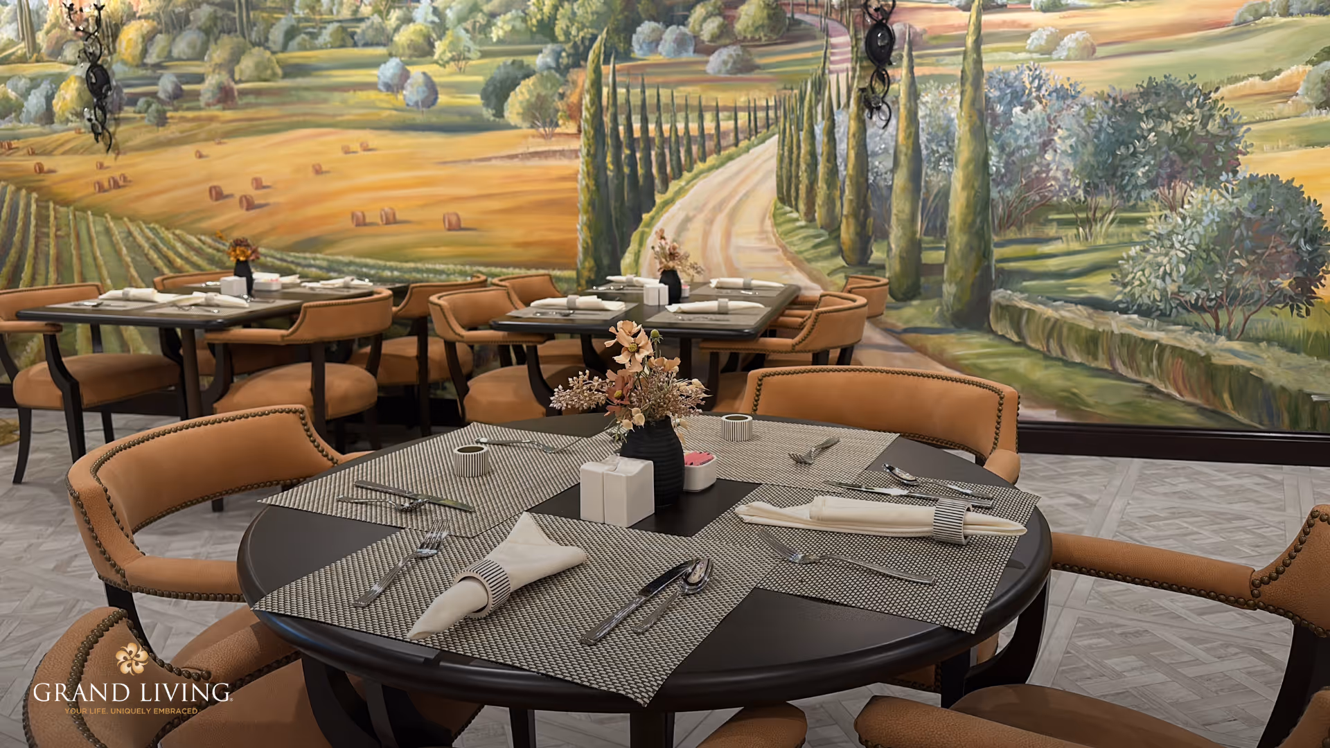 A dining room with round tables set for meals, upholstered chairs, and a large countryside mural on the wall.