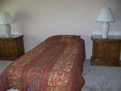 A single bed with red patterned quilt flanked by two wooden nightstands and lamps.