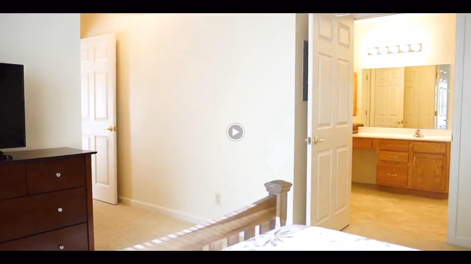 Bedroom showing a dresser and bed frame with an open door leading to a bathroom vanity and mirror.
