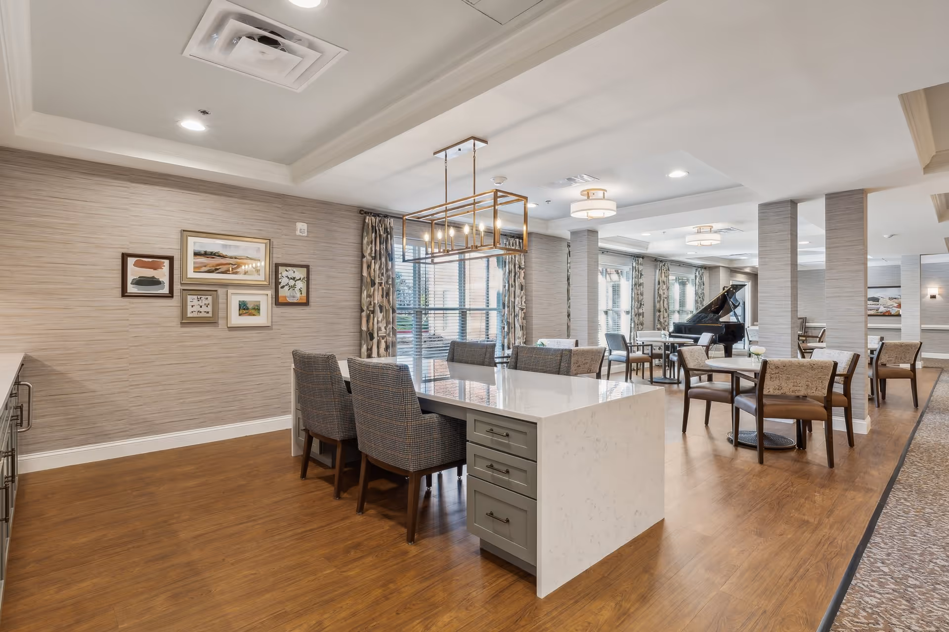 Communal dining area with a central marble-topped island, multiple tables and chairs, and a grand piano in the background.