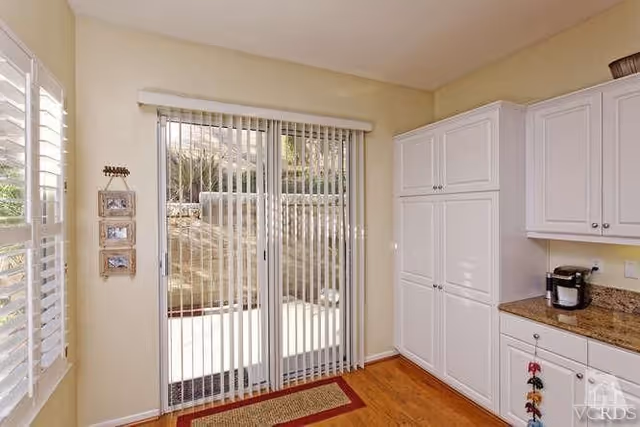 Bright kitchen nook with white cabinets, a granite countertop and a sliding glass door with vertical blinds leading outside.