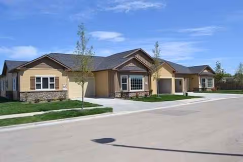 Single-story senior living facility exterior with beige siding, stone accents, and a curved driveway.