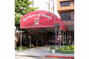 Entrance to the Brothers of Mercy facility with a maroon awning displaying the facility name and logo, surrounded by plants and adjacent to a multi-story building.