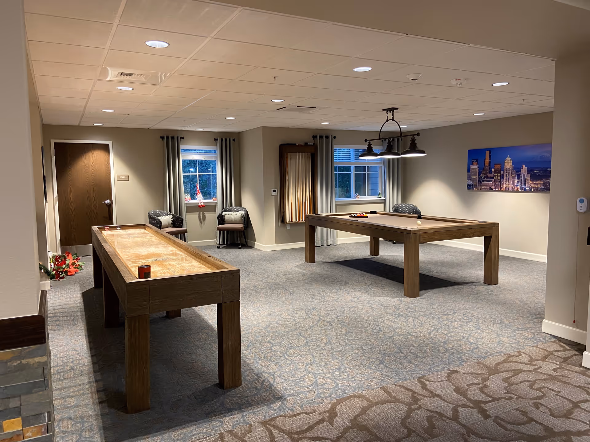 Spacious interior game room with a pool table, shuffleboard table, seating and cityscape artwork.