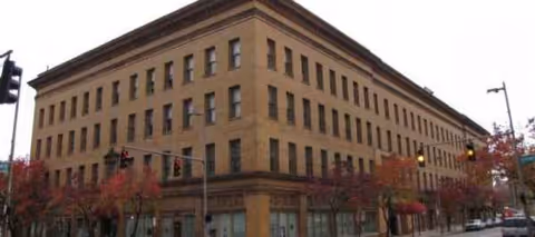 A large brick, multi-story building on a street corner with trees.