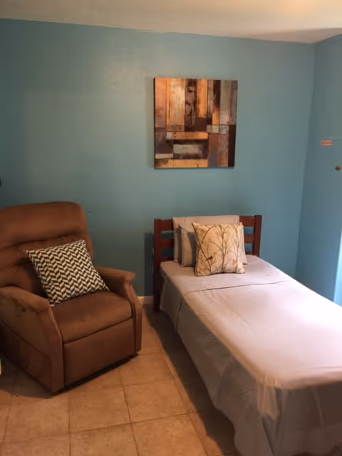 Small bedroom with a single bed, a brown recliner chair, teal walls, and a piece of wall art.