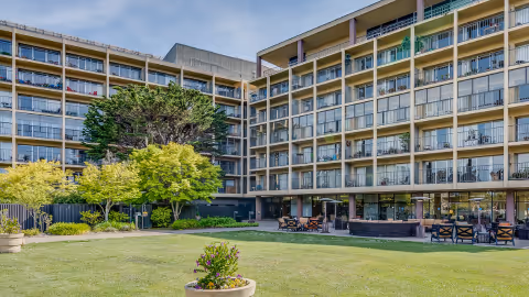 Exterior view of a multi-story senior living building with balconies overlooking a grassy courtyard and outdoor seating.