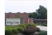 Brick single-story care facility front with landscaped shrubs, a driveway, and an entrance sign reading 'Shady Oaks'.
