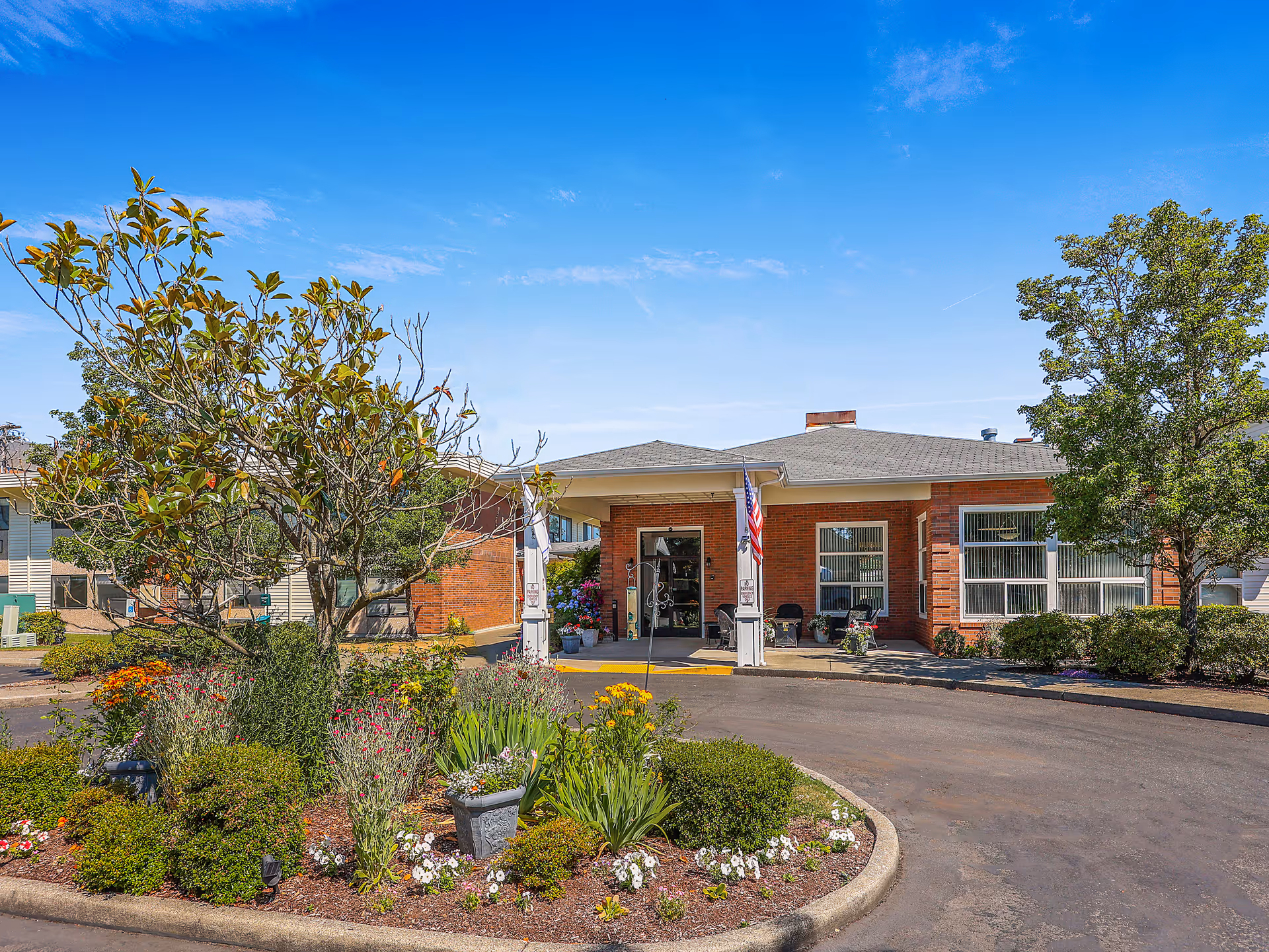 Exterior view of the White River Assisted Living facility surrounded by colorful flowers and trees.