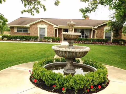Front view of a brick senior living facility with a tiered fountain and manicured lawn.