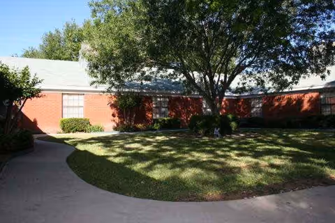 Exterior view of a single-story brick building with a curved walkway and grassy lawn.